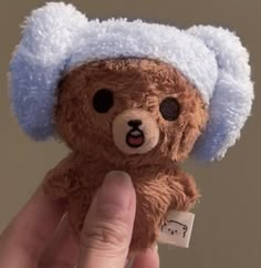 a hand holding a brown teddy bear with a blue hat on it's head