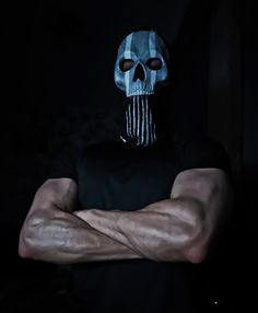 a man with his arms crossed in front of him, wearing a black shirt and skull mask