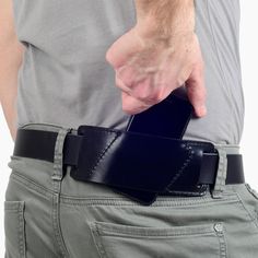 a man is holding his cell phone in his back pocket while wearing a leather belt