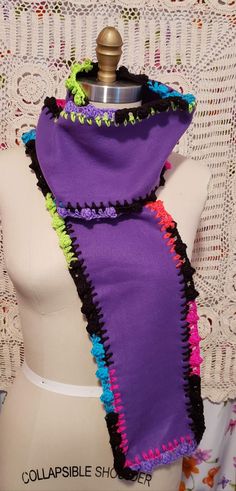 a mannequin wearing a purple scarf with multicolored crochet trim