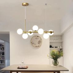 a dining room table with four lights hanging from it's ceiling and two vases on the other side