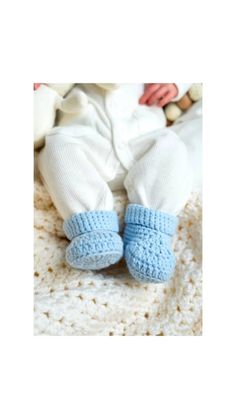 a baby laying on top of a white blanket wearing blue knitted slippers and socks