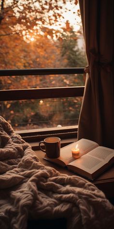 an open book and cup on a window sill with the sun setting in the background