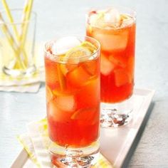 two glasses filled with drinks sitting on top of a white tray next to each other