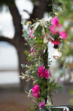 pink flowers and greenery are hanging from a metal pole in front of a tree