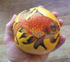 a hand holding an orange with a goldfish painted on it