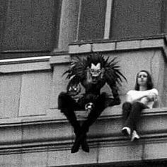 black and white photograph of two people sitting on the ledge of a building with an evil looking face