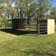 a horse pen in the middle of a grassy field with trees and grass around it