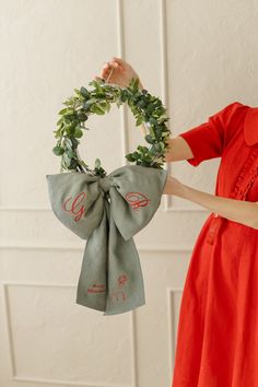 a woman is holding a wreath with the letter s on it and wearing a red dress