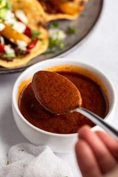 a spoon is being used to dip sauce in a bowl with tortilla bread on the side