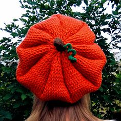 a woman wearing an orange knitted beanie with a green leaf on the top