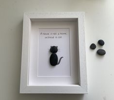 a black cat sitting in a white frame next to some rocks on the wall with a quote above it