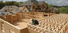 a man working on the roof of a house under construction in front of other houses