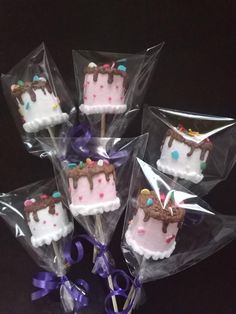 six decorated birthday cake pops in plastic wrappers on a black table with purple ribbon