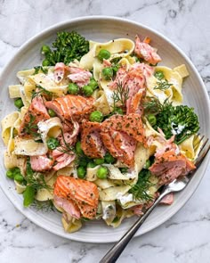 a white plate topped with pasta, salmon and veggies next to a fork