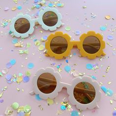 two yellow and white sunglasses sitting next to each other on a pink surface with confetti