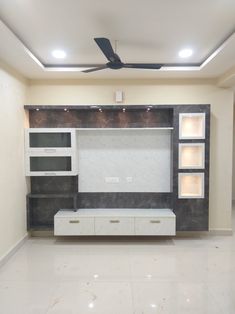 an empty living room with white cabinets and black ceiling fan in the center, along with built - in shelving units