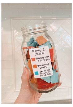 a person holding a jar filled with colorful pieces of paper and some words on it