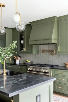 a green kitchen with marble counter tops and gold pulls on the cabinetry, along with hanging lights