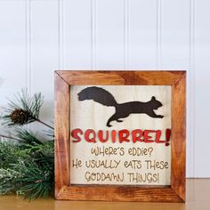 a wooden frame with a squirrel sign in it on a table next to pine branches