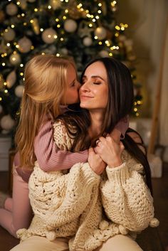 a mother and daughter kissing in front of a christmas tree