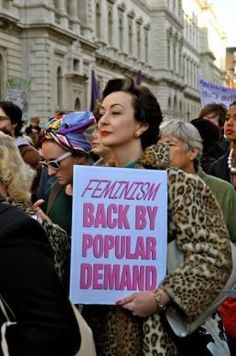 a woman holding a sign that says feminist back by popular demand