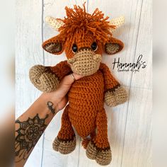 a hand holding a small stuffed animal in the shape of a cow on a white wooden background