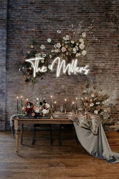 a table with candles and flowers on it in front of a brick wall that is decorated with greenery