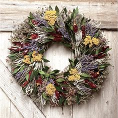 a wreath is hanging on the side of a wooden door with dried flowers and leaves