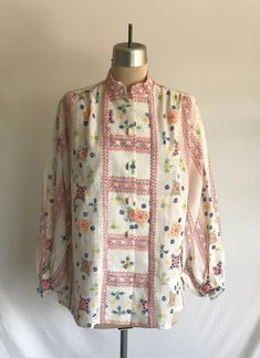 Great 1970's semi-sheer cotton smock style blouse with banded collar, front wooden toggle buttoning placket and the best faux embroidered Scandinavian print! This blouse is perfect for spring or summer! Blouse is clean and in excellent condition - please note it does have a perfume-y smell to it. This may disappear with wear and another wash.  Label: Lady Arrow  Measurements: would best fit a modern size M Bust= 45" Bottom opening= 48" Shoulder width= 17 1/2" Sleeve length= 21" Bicep= 19 1/4" Sl Vintage Spring Blouse With Chikankari Embroidery, Vintage Blouse With Chikankari Embroidery For Spring, Vintage Chikankari Embroidery Blouse For Spring, Collared Blouse With Floral Embroidery For Daywear, Floral Embroidered Collar Blouse For Daywear, Floral Embroidery Collar Blouse For Daywear, Daywear Blouse With Floral Embroidery And Collar, Floral Embroidery Blouse With Collar For Daywear, Traditional Tops With Buttons For Spring