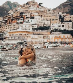 two people in the water hugging each other with buildings in the back ground behind them