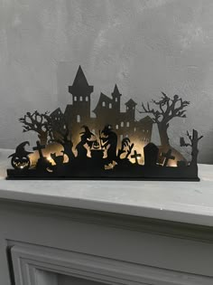 an illuminated halloween scene with pumpkins, bats and witches on a mantle in front of a gray wall