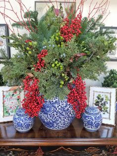 a blue and white vase sitting on top of a table next to pictures with red berries