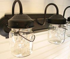 three mason jars are hanging on the wall next to a light fixture with two lights