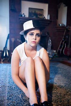 a woman sitting on the floor with her legs crossed wearing black shoes and a hat