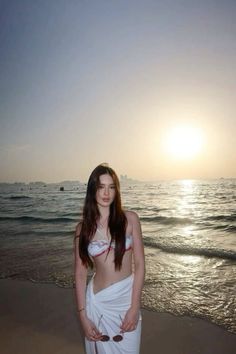 a woman standing on top of a sandy beach next to the ocean at sun set