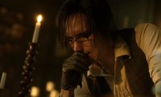 a man with glasses holding a candle in his hand and looking at something on the table