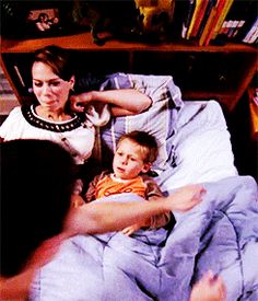 a woman laying in bed next to a little boy with his arm wrapped around him