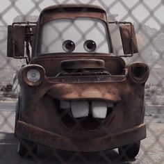 the character mater from cars is smiling behind a chain link fence