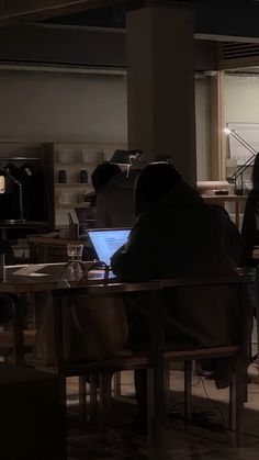 two people sitting at a table working on laptops in a dark room with windows