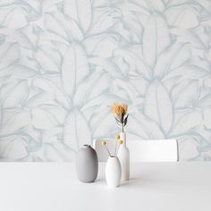 two vases with flowers are sitting on a table in front of a wallpapered background