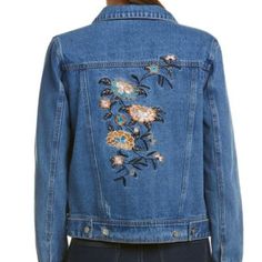 a woman wearing a jean jacket with embroidered flowers on the front and back of it