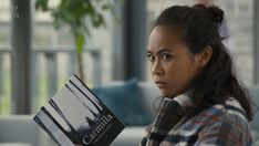 a woman sitting on a couch holding a book in her hand and looking at the camera