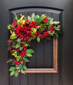 a wreath with red flowers and green leaves hanging on a door