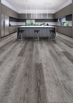 a large kitchen with wooden floors and gray cabinets is pictured in this image, there are two stools at the center of the room