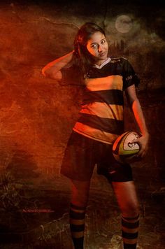 a woman holding a soccer ball in her right hand and posing for the camera with an intense look on her face