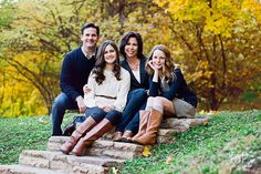 four people sitting on steps in front of trees with fall foliage behind them, posing for a family photo