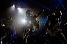 three people in masks are playing guitars on stage with lights behind them and one person wearing a mask