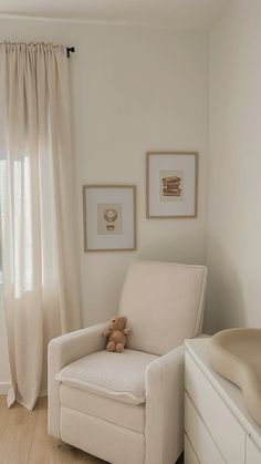 a baby's room with a white chair and pictures on the wall