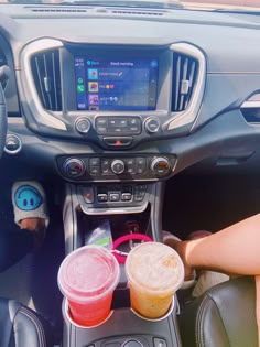 the interior of a car with two drinks in plastic cups on the center console, and someone's feet propped up against the steering wheel